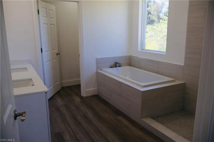 Bathroom with double vanity, a garden tub, and dark wood finished floors