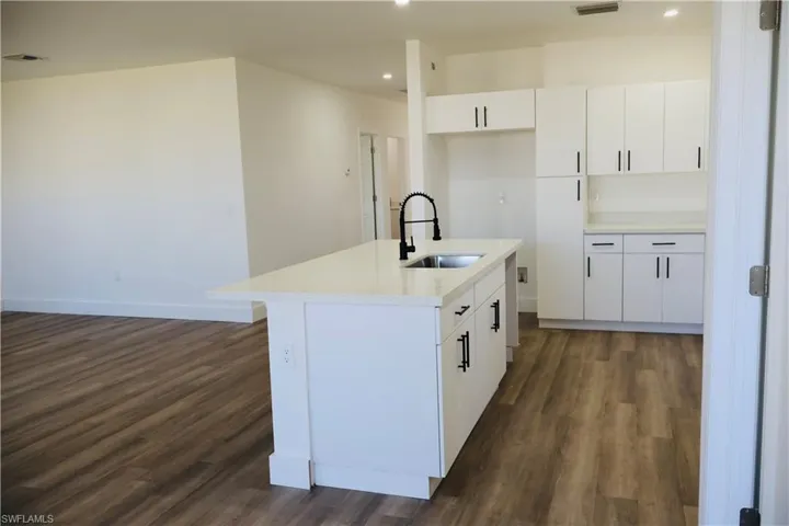 Kitchen featuring white cabinetry, dark wood-style flooring, a center island with sink, recessed lighting, and light stone countertops