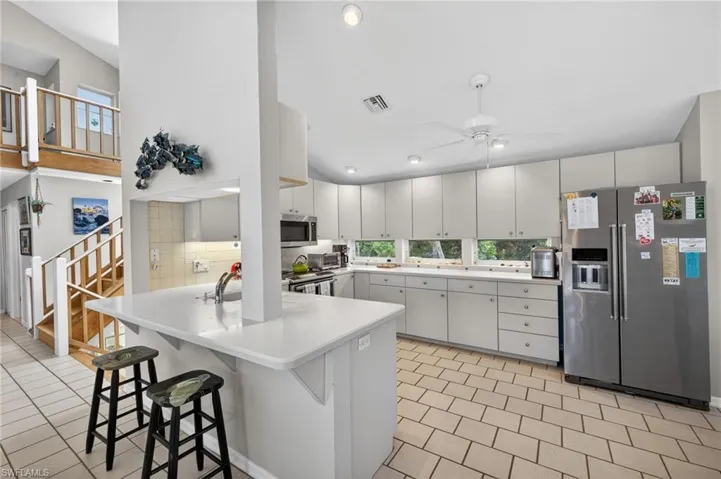 Kitchen featuring stainless steel appliances, light countertops, a kitchen breakfast bar, white cabinetry, and ceiling fan