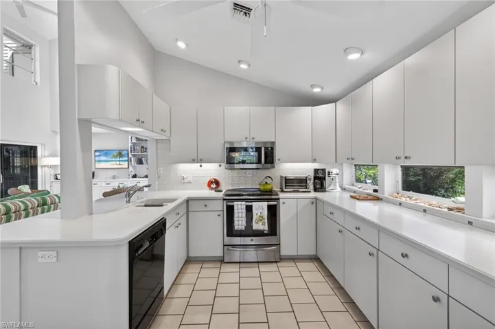Kitchen featuring a peninsula, vaulted ceiling, stainless steel appliances, white cabinets, and decorative backsplash