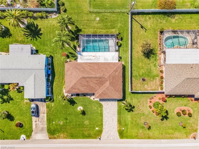 Bird's eye view of a pool enclosure and yard with partial fencing and tropical landscape