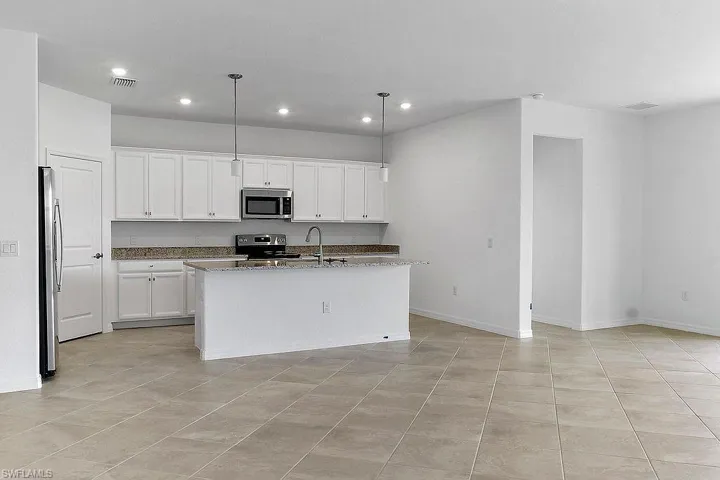 Open-concept kitchen featuring white cabinetry, stainless steel appliances, granite countertops, and a central island with pendant lighting