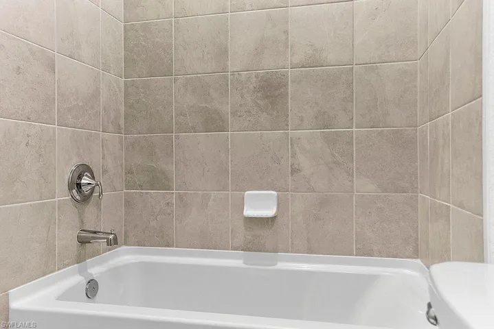 Bathtub with polished chrome fixtures, featuring a tiled surround in neutral tones