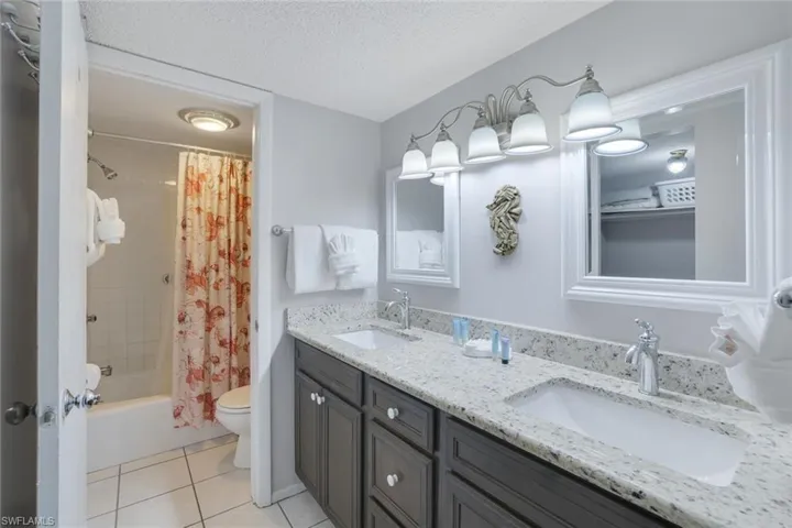 Full bathroom featuring toilet, a textured ceiling, vanity, shower / bathtub combination with curtain, and tile patterned flooring