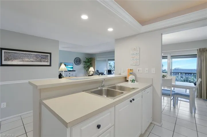 Kitchen featuring light tile patterned flooring, sink, white cabinets, white dishwasher, and kitchen peninsula