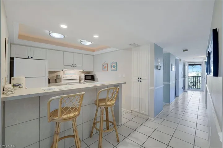 Kitchen featuring a breakfast bar area, white cabinets, kitchen peninsula, a raised ceiling, and white appliances
