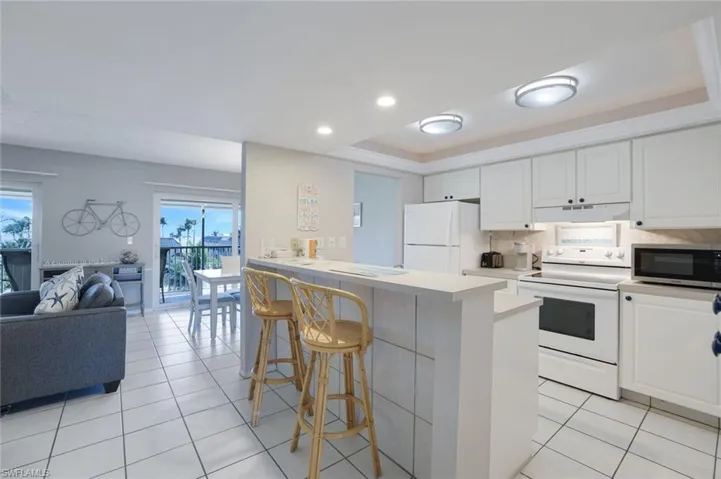 Kitchen featuring a tray ceiling, white appliances, white cabinets, and light tile patterned flooring