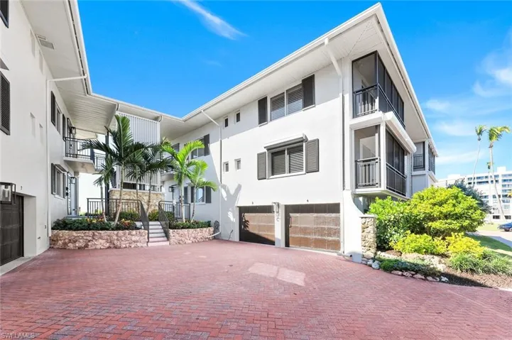 View of front facade featuring an attached garage, a balcony, stucco siding, decorative driveway, and stairway