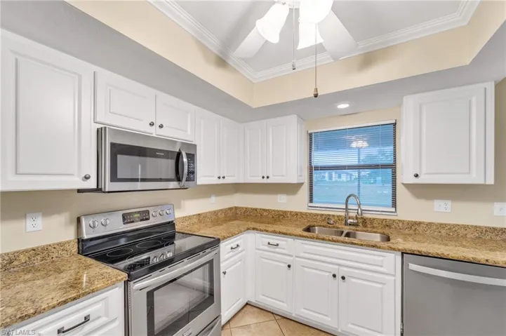 Kitchen featuring appliances with stainless steel finishes, light stone countertops, ornamental molding, and white cabinets
