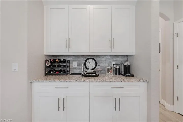 Bar featuring light stone countertops, light hardwood / wood-style flooring, white cabinets, and tasteful backsplash