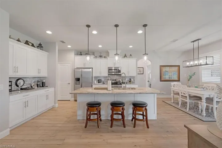 Kitchen with decorative light fixtures, white cabinets, backsplash, and appliances with stainless steel finishes