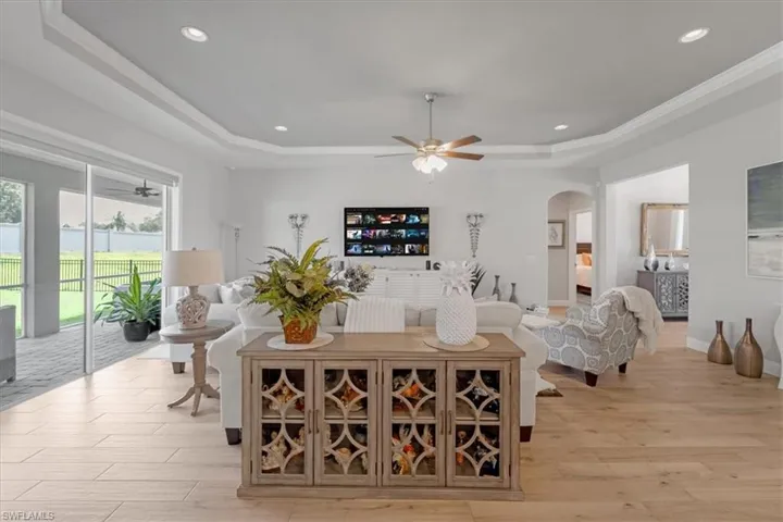 Living room featuring ceiling fan, ornamental molding, a tray ceiling, and light hardwood / wood-style floors