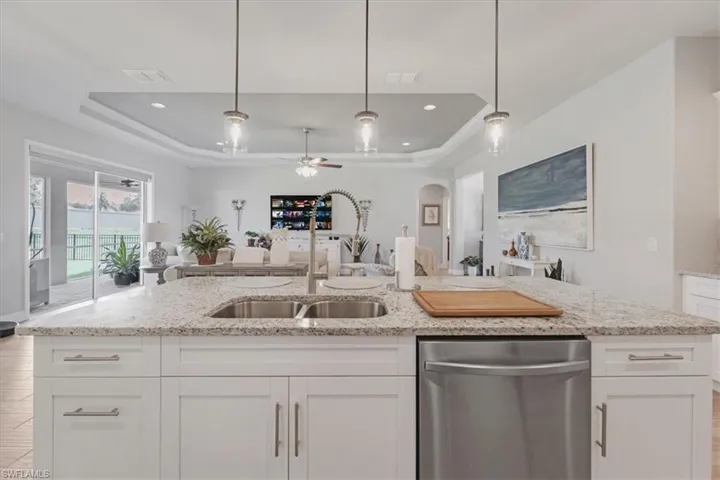 Kitchen featuring ceiling fan, a tray ceiling, dishwasher, decorative light fixtures, and white cabinets