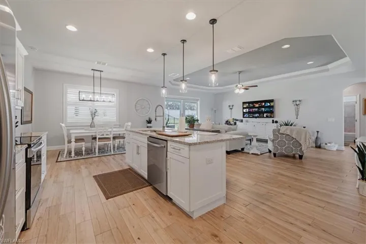 Kitchen featuring white cabinetry, light wood-type flooring, stainless steel appliances, ceiling fan, and a raised ceiling