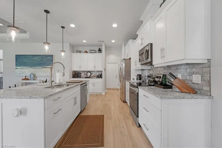 Kitchen featuring white cabinetry, hanging light fixtures, light hardwood / wood-style flooring, stainless steel appliances, and tasteful backsplash