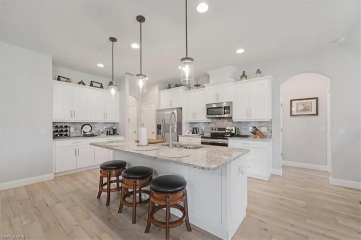 Kitchen featuring backsplash, appliances with stainless steel finishes, pendant lighting, and white cabinets