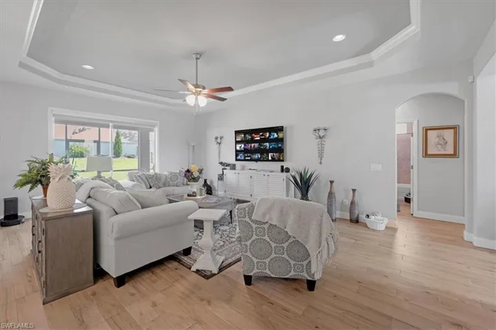 Living room featuring ceiling fan, a tray ceiling, and light wood-type flooring