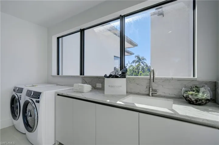 Laundry area with washer and dryer, light tile patterned flooring, cabinets, and sink