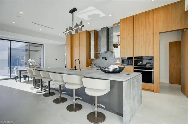 Kitchen featuring pendant lighting, wall chimney exhaust hood, decorative backsplash, and a large island with sink
