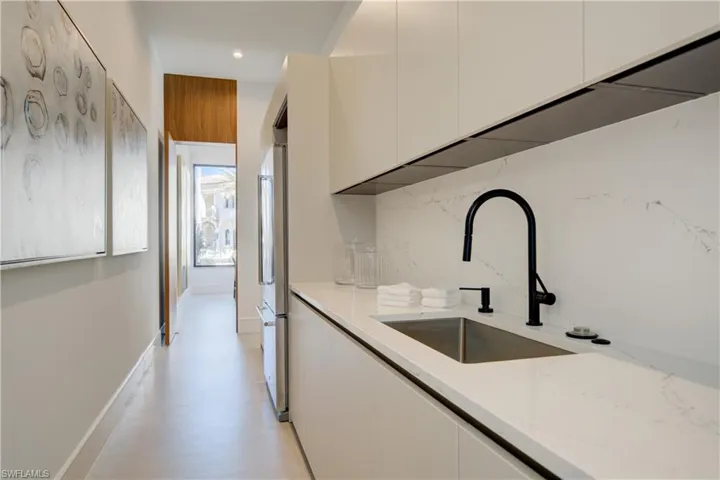 Kitchen featuring light stone countertops, light wood-type flooring, tasteful backsplash, sink, and white cabinetry