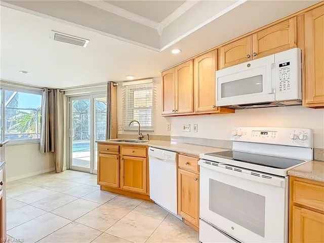 Kitchen with white appliances, light tile patterned floors, recessed lighting, light brown cabinets, and ornamental molding