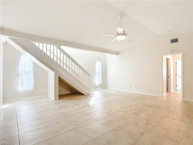 Spare room with stairway, vaulted ceiling, light tile patterned floors, and a ceiling fan