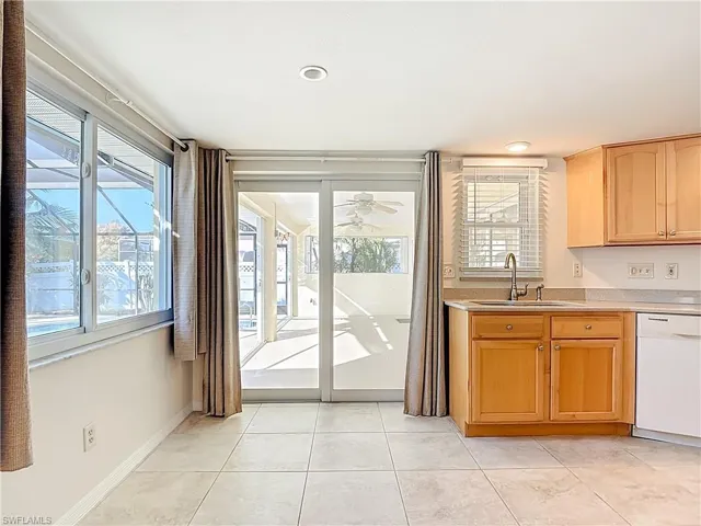 Kitchen featuring white dishwasher, light tile patterned flooring, and light stone countertops