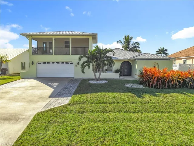 View of front facade with stucco siding, driveway, a metal roof, and a front lawn