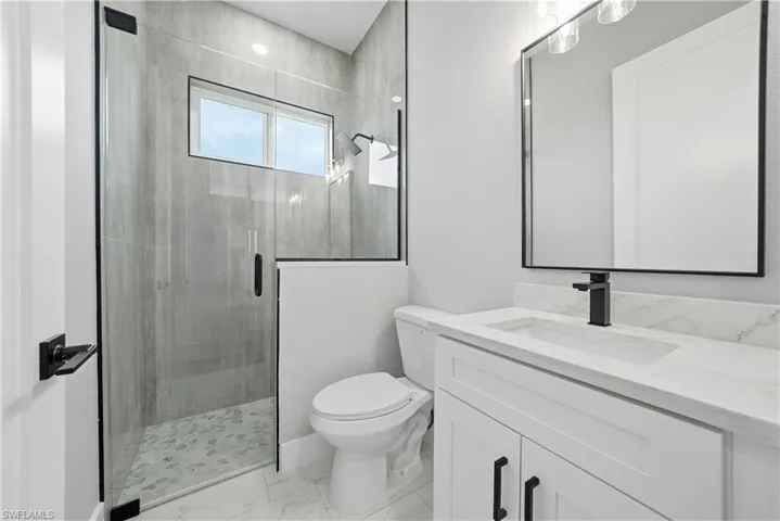 Full bath featuring a shower stall, vanity, and light marble finish flooring
