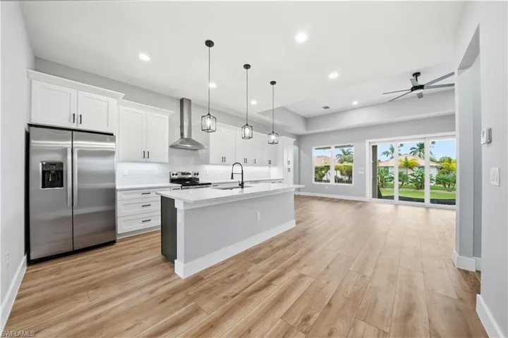 Kitchen with stainless steel appliances, white cabinets, decorative light fixtures, open floor plan, and a kitchen island with sink