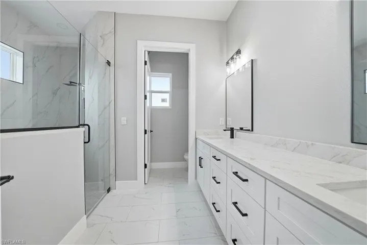 Bathroom featuring a marble finish shower, double vanity, and light marble finish flooring