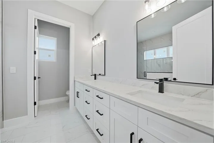 Bathroom with a marble finish shower, double vanity, and light marble finish floors