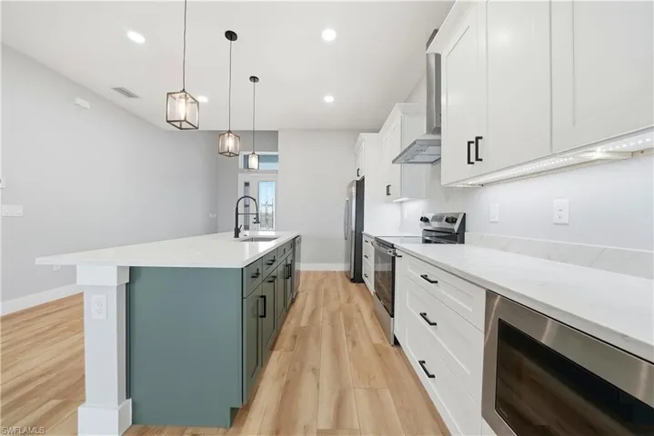 Kitchen featuring dual tone cabinets, stainless steel appliances, pendant lighting, light stone counters, and a center island with sink