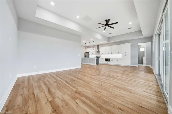 Unfurnished living room featuring a raised ceiling, ceiling fan, light wood finished floors, and recessed lighting