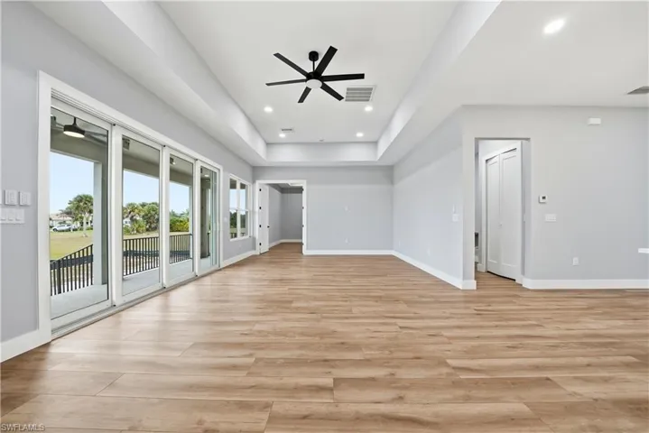 Unfurnished living room with ceiling fan, light wood-type flooring, recessed lighting, and a tray ceiling