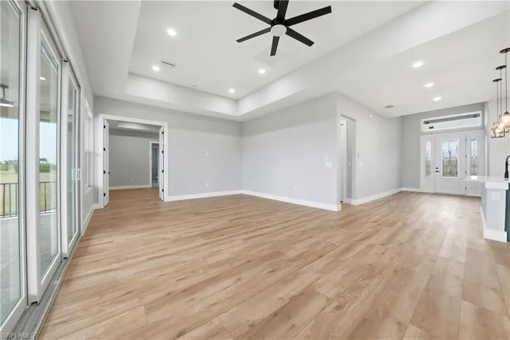 Unfurnished living room featuring a ceiling fan, light wood-style flooring, recessed lighting, and a tray ceiling