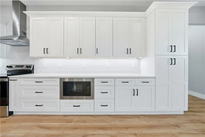 Kitchen featuring electric stove, white cabinets, built in microwave, and light wood-style flooring