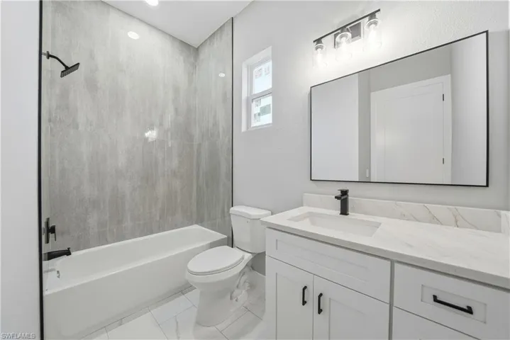 Bathroom with washtub / shower combination, vanity, and light marble finish flooring