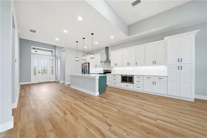 Kitchen featuring an island with sink, hanging light fixtures, light wood-style flooring, stainless steel appliances, and open floor plan