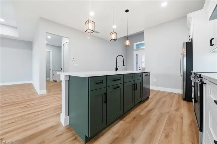 Two tone kitchen with an island with sink, two tone cabinetry, light wood-style floors, hanging light fixtures, and stainless steel appliances