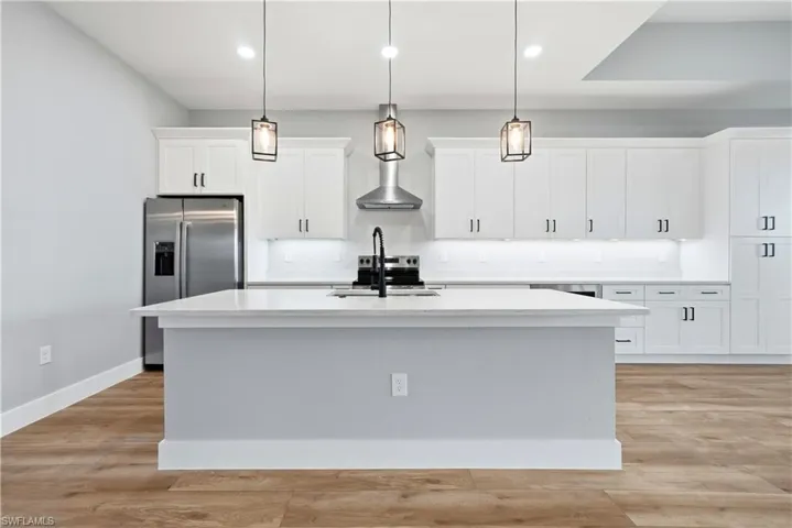 Kitchen with light wood-type flooring, stainless steel appliances, white cabinetry, and pendant lighting