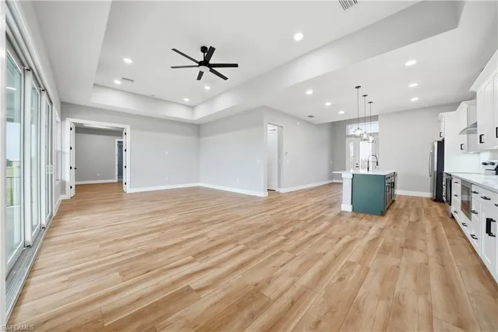 Unfurnished living room featuring a ceiling fan, light wood-style floors, plenty of natural light, recessed lighting, and a tray ceiling