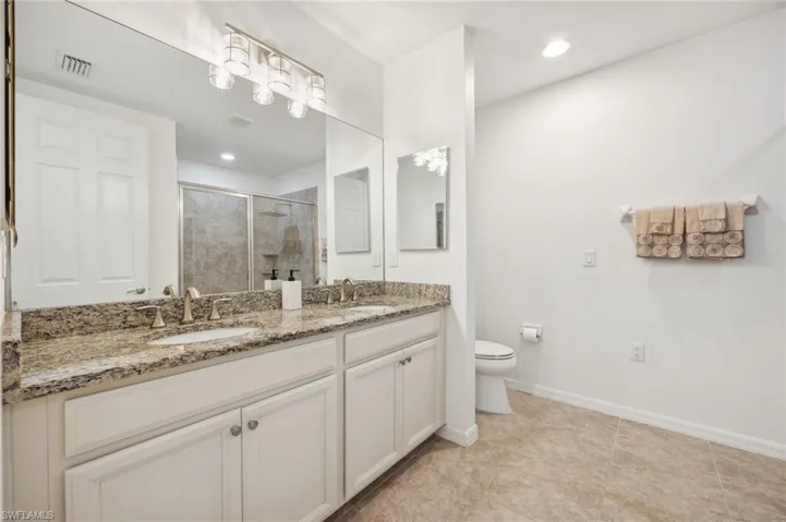 Bathroom with tile flooring, oversized vanity, double sink, and toilet