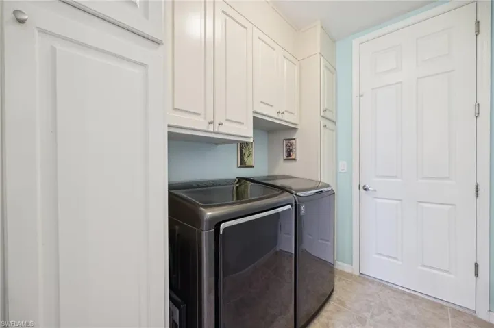 Washroom with cabinets, light tile floors, and washing machine and dryer
