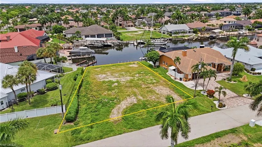 Cleared residential lot with canal frontage, featuring a manicured grassy area and mature palm trees