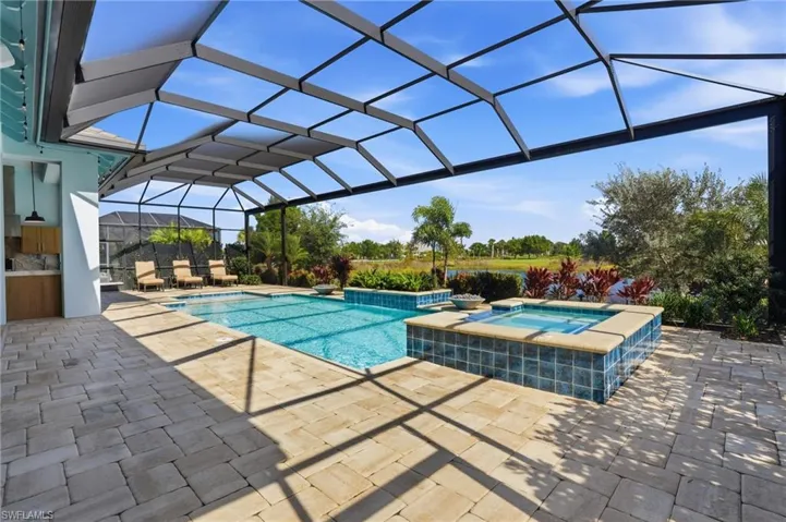 Screened-in pool area featuring a spillover spa, paver patio, built-in outdoor cabinetry, and tile water features