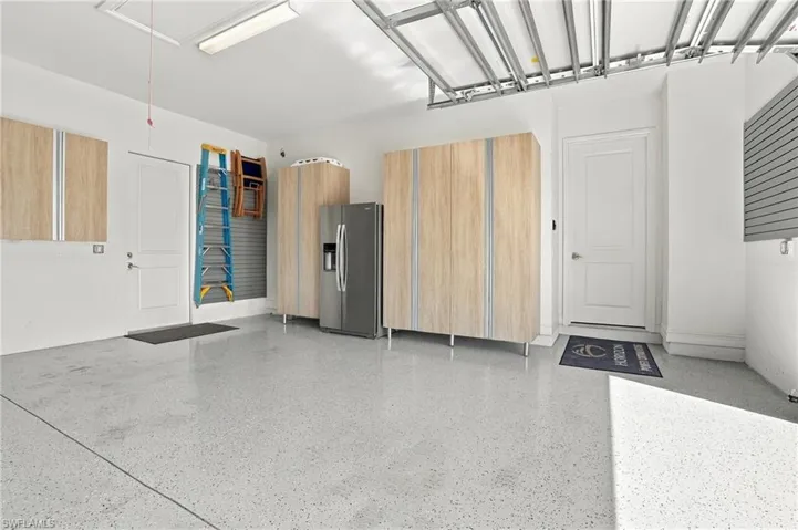 Finished garage featuring epoxy flooring, built-in light-tone cabinetry, and wall-mounted storage panels