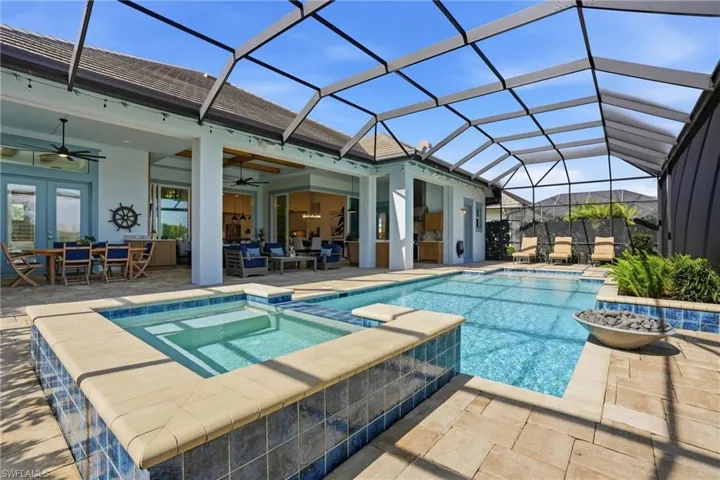 Screen-enclosed patio featuring a paver deck, built-in spa, swimming pool with tiled coping, and covered outdoor area