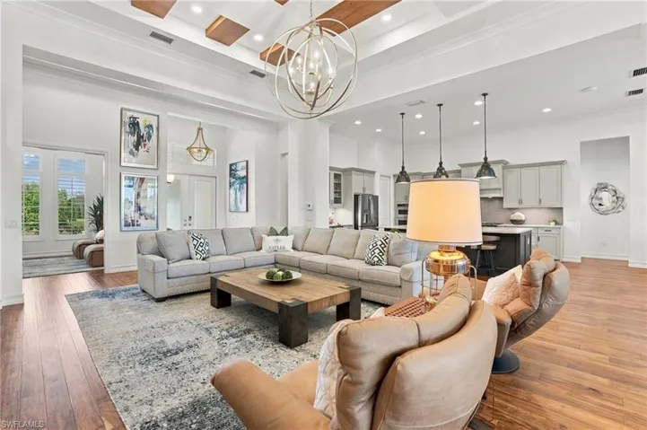 High ceilings featuring tray accents and exposed wood beams, open-concept kitchen with shaker-style cabinetry, large kitchen island with pendant lighting, and wide-plank wood-finish flooring