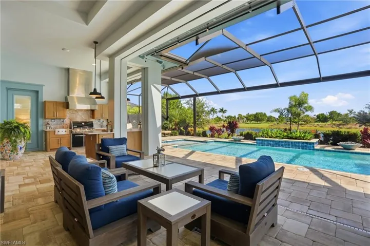 Covered lanai featuring a stone paver floor, built-in outdoor kitchen with stainless steel appliances, retractable screen enclosure, and swimming pool with a raised water feature